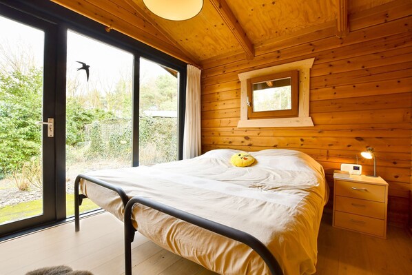 A wooden cabin bedroom with a bed, a nightstand, and a window. - Wooden Holiday Home in Meijel With Private Garden (Meijel)