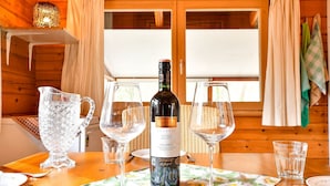 A wooden cabin interior with a dining table set for a meal, featuring a bottle of wine, wine glasses, and a pitcher. - Wooden Holiday Home in Meijel With Private Garden (Meijel)