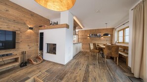 A modern living room with wooden flooring, a fireplace, a television, and a dining area with chairs and a table. - Affluent Chalet in Neukirchen near Wildkogel Ski Arena (Neukirchen am Grossvenediger)