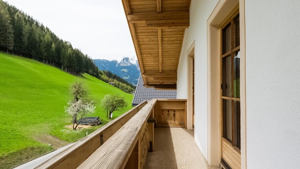 Un balcon doté d’une balustrade en bois, offrant une vue sur une colline verdoyante et une chaîne de montagnes.