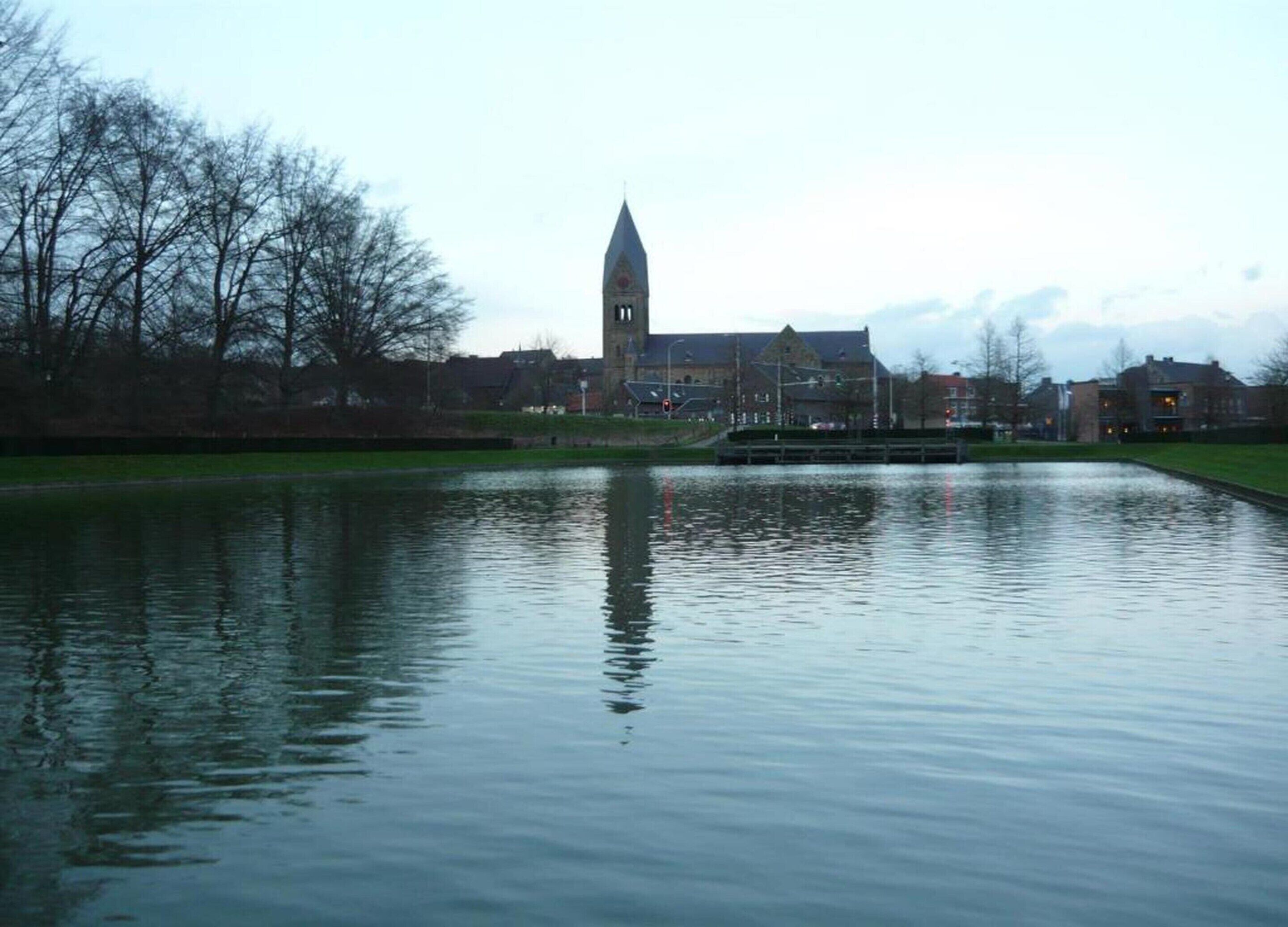 Een kalm wateroppervlak met een kerktoren in de verte.