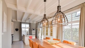 A dining area with a wooden table, orange chairs, and pendant lights. - Great Holiday Home at the Efteling with Heated Swimming Pool & Hot Tub (Kaatsheuvel)