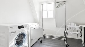 A laundry room with a front-loading Miele washing machine, a drying rack, and a small table with a chair. - Great Holiday Home at the Efteling with Heated Swimming Pool & Hot Tub (Kaatsheuvel)