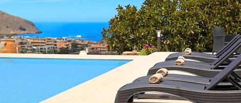 A poolside area with lounge chairs and a view of the ocean and buildings in the background.