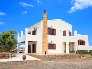 Une maison moderne à deux étages, dotée d’une cheminée en pierre, de murs blancs et de volets bruns.