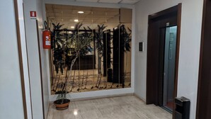 Un couloir avec un mur recouvert de miroirs qui reflète un paysage tropical, un extincteur et un ascenseur.