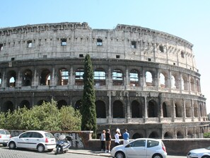 A historic coliseum with multiple arches and columns, surrounded by parked cars and a few people. - Snug Apartment in Roma near San Giovanni Train Station (Rome)
