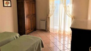 A room with two beds, a wooden wardrobe, a radiator, and a window with sheer curtains. - Belvilla by OYO Tenute D'angelo (Agrigento)