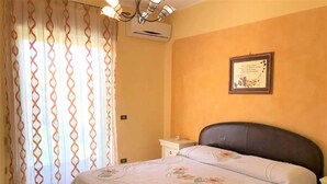 A bedroom with a bed, curtains, an air conditioning unit, and a framed picture on the wall. - Belvilla by OYO Tenute D'angelo (Agrigento)