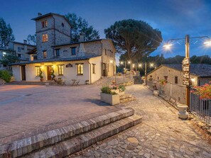 A stone building with a tower, a paved courtyard, and outdoor seating. - Belvilla by OYO Appartamento Garden 3 pax (Montone)