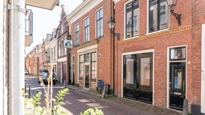 Une ruelle étroite pavée de briques, bordée de bâtiments des deux côtés, avec une porte noire et une boîte aux lettres.