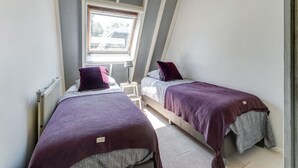 Une chambre avec deux lits, une lucarne et un radiateur.