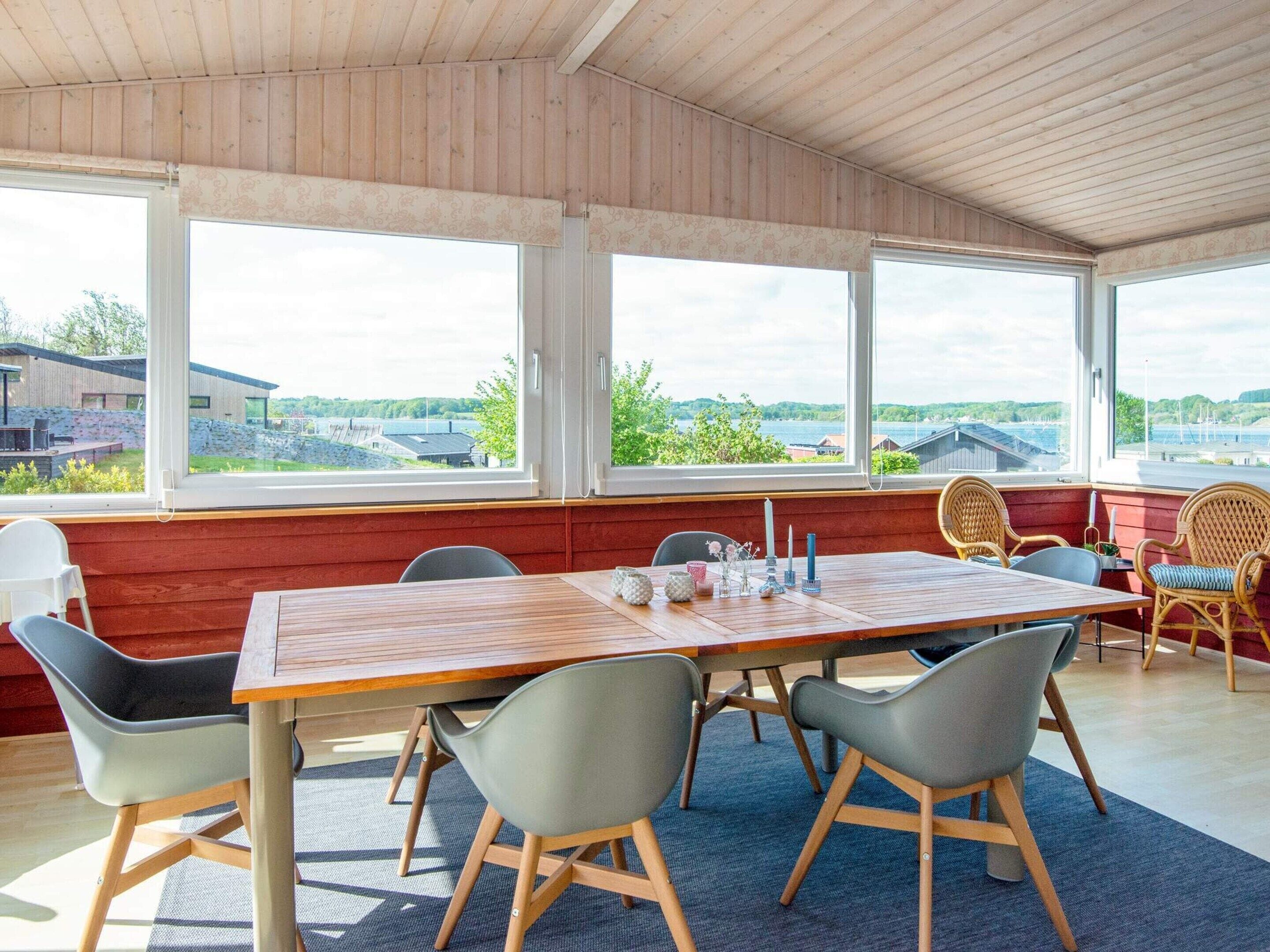 A dining area with a wooden table and chairs, large windows with a view of a landscape, and a red wall.