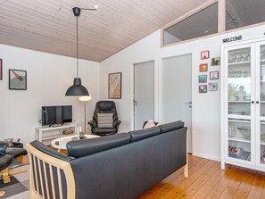A modern living room with a black leather sofa, a television, a black pendant light, and a cabinet with glass doors.