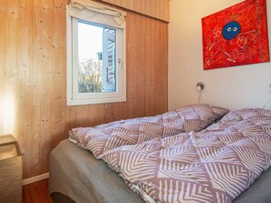 A bedroom with a wooden wall, a window with a curtain, a bed with patterned bedding, and a red abstract painting on the wall. - 4 Person Holiday Home in Haderslev (Haderslev)