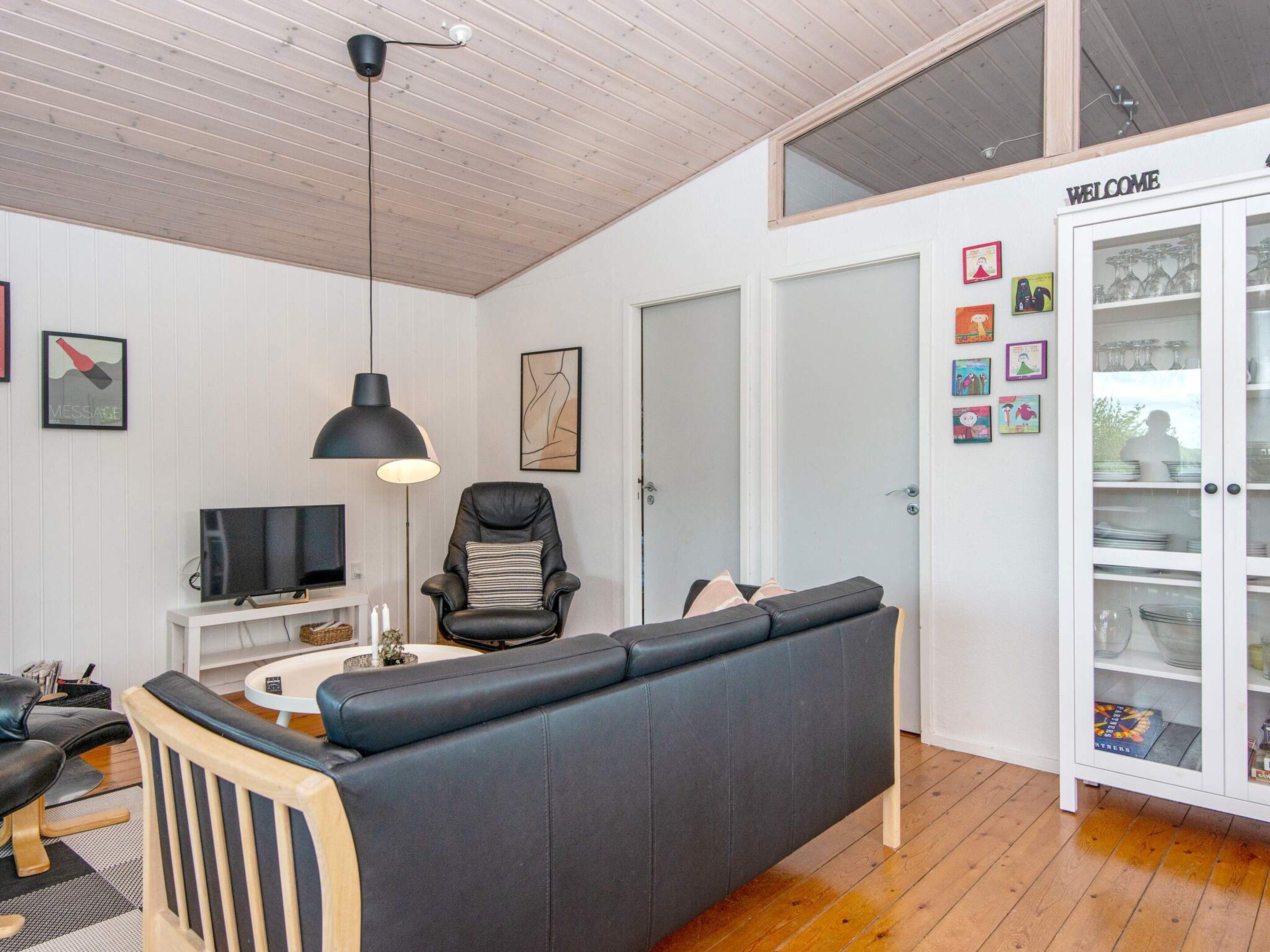 A modern living room with a black leather sofa, a television, a black pendant light, and a cabinet with glass doors.