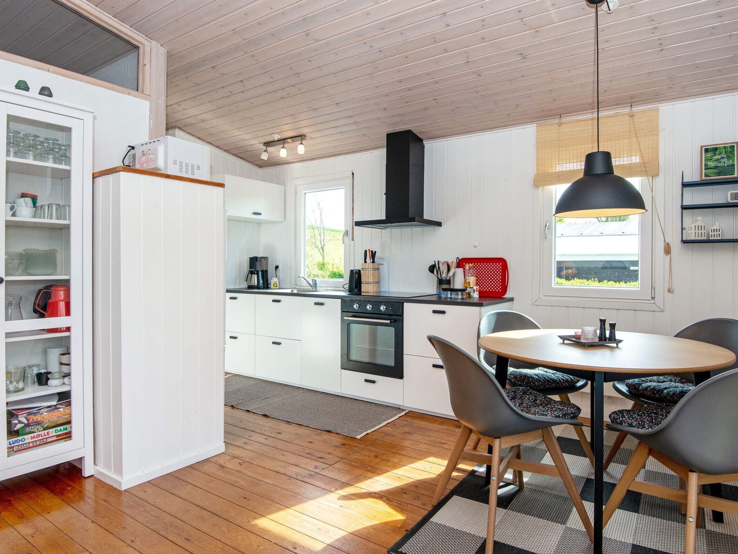 A modern kitchen with white cabinetry, a black stove, and a dining area with a round table and chairs.