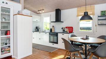 A modern kitchen with white cabinetry, a black stove, and a dining area with a round table and chairs.