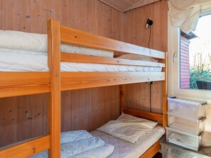A bunk bed with a wooden frame and white bedding, a window with a view of greenery, and a plastic storage unit with drawers. - 4 Person Holiday Home in Haderslev (Haderslev)