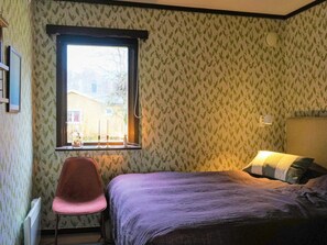 Un dormitorio con cama, una silla, un ventanal y un radiador.