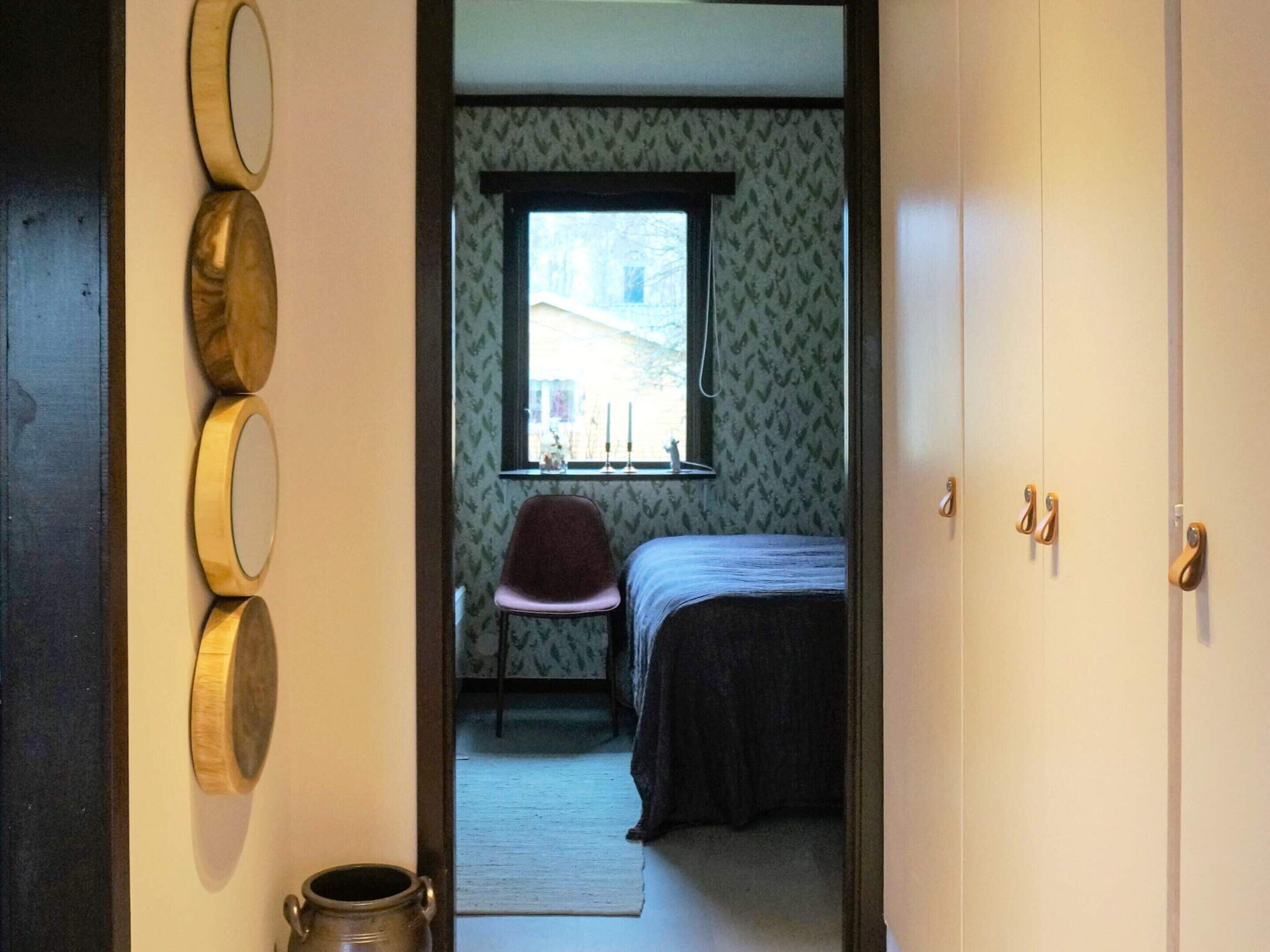 A bedroom with a bed, a chair, a window, and a mirror on the wall.