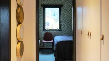Ein Schlafzimmer mit einem Bett, einem Sessel, einem Fenster und einem Spiegel an der Wand.