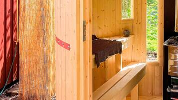 A wooden sauna room with a bench, a small window, and a sauna heater.