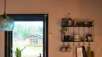Ein Zimmer mit Fenster, einer Pendelleuchte, einem Regal mit Küchenutensilien und einer kleinen Pflanze.