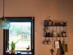 A room with a window, a hanging light fixture, a shelf with kitchenware, and a small plant. - 4 Person Holiday Home in Tibro (Tibro)