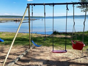 A swing set with two swings, a wooden frame, and a view of a lake. - 4 Person Holiday Home in Tibro (Tibro)