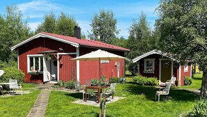A red wooden house with a covered patio, a stone pathway, and a small garden. - 4 Person Holiday Home in Tibro (Tibro)