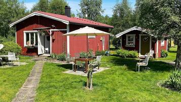 A red wooden house with a covered patio, a stone pathway, and a small garden.