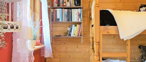 A wooden bunk bed room with a bookshelf, lace curtains, and a fan.