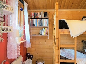 Dormitorio con literas de madera, una estantería, cortinas de encaje y un ventilador.