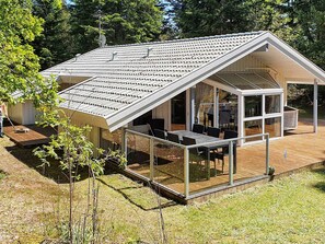 Et moderne hus med skråt tag, en overdækket terrasse med bord og stole, samt et glasindhegnet område.