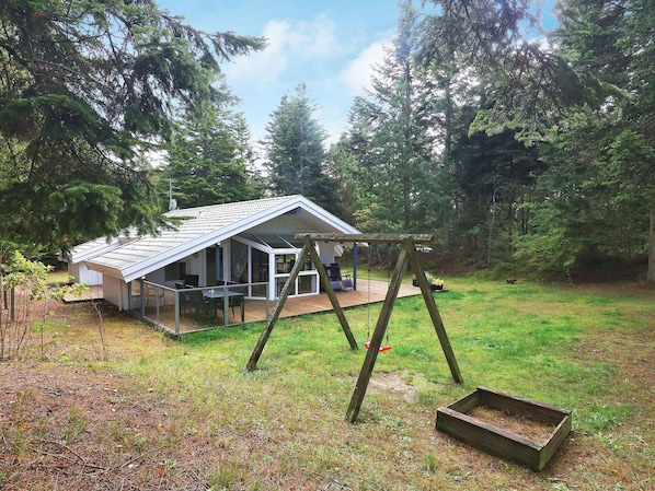 A cabin with a covered patio, a swing set, and a wooden deck.