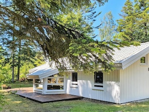A small, single-story cabin with a sloped roof, a front porch, and a deck area.