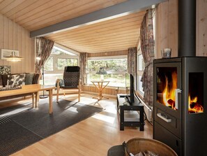 Ein gemütliches Wohnzimmer mit Holzboden, einer Couch, einem Esstisch, einem Fernseher und einem Kaminofen.