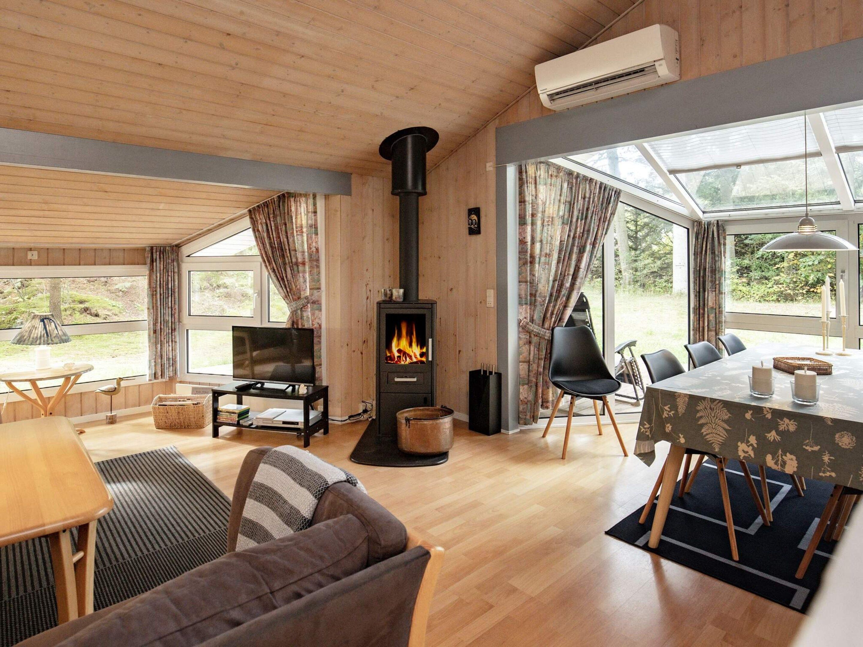 A cozy living room with a fireplace, wooden furniture, and large windows.