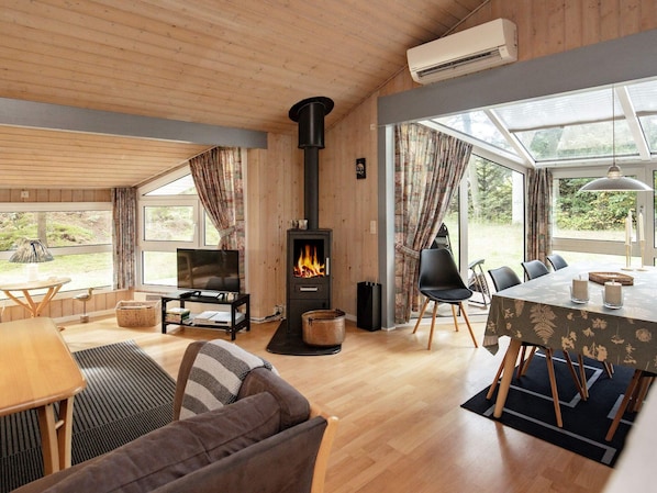 A cozy living room with a fireplace, wooden furniture, and large windows.