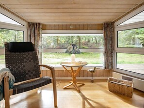 A room with a large window, a wooden ceiling, a black and white patterned chair, a small round table with a candle, and a wicker basket. - Holiday Home in Saltum (Saltum)