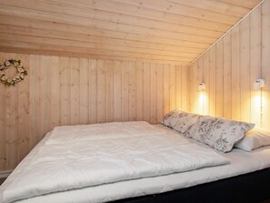 A room with wooden panel walls, a bed with white bedding, and two wall-mounted lamps.