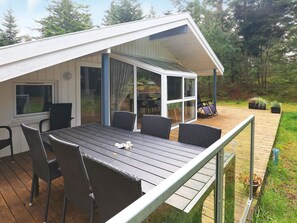 A covered outdoor seating area with a table and chairs, a glass door leading to a patio, and a wooden deck. - Holiday Home in Saltum (Saltum)