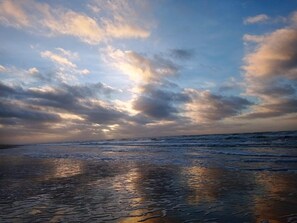 A beach with wet sand and a cloudy sky.
