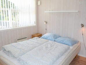 Uma cama com um edredom listrado, uma mesa de cabeceira e um abajur fixado na parede.