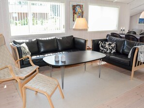 A living room with a black leather sofa, a wooden chair, a small table with two candles, and a lamp. - Holiday Home in LÃ¸kken (Lokken)