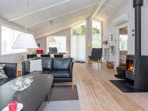 A modern living room with a fireplace, leather sofa, dining table, and a large window. - Holiday Home in LÃ¸kken (Lokken)
