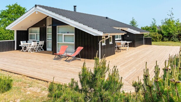 A modern house with a wooden deck, two outdoor seating areas, and a large window.