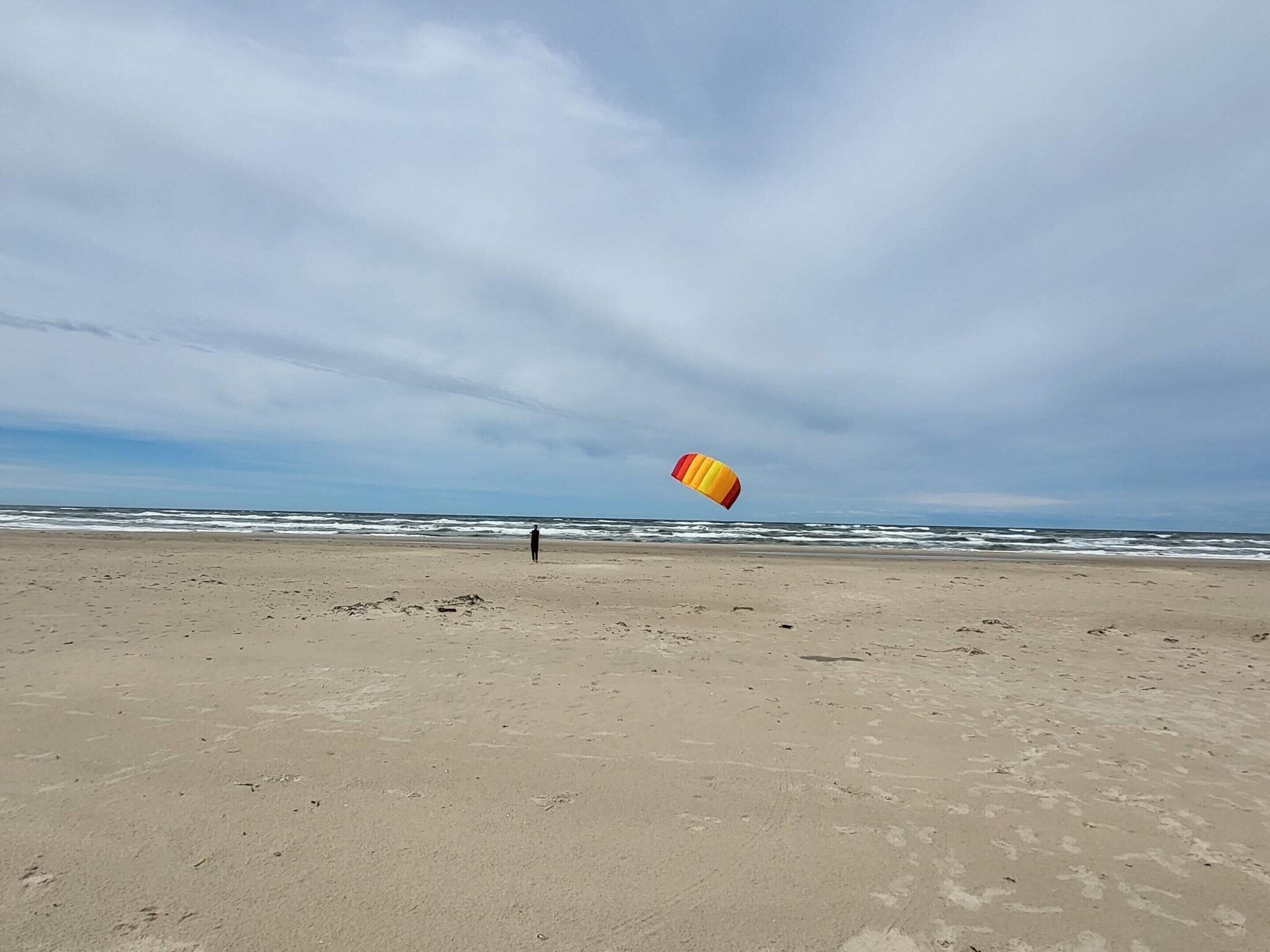 A beach with a person flying a kite.