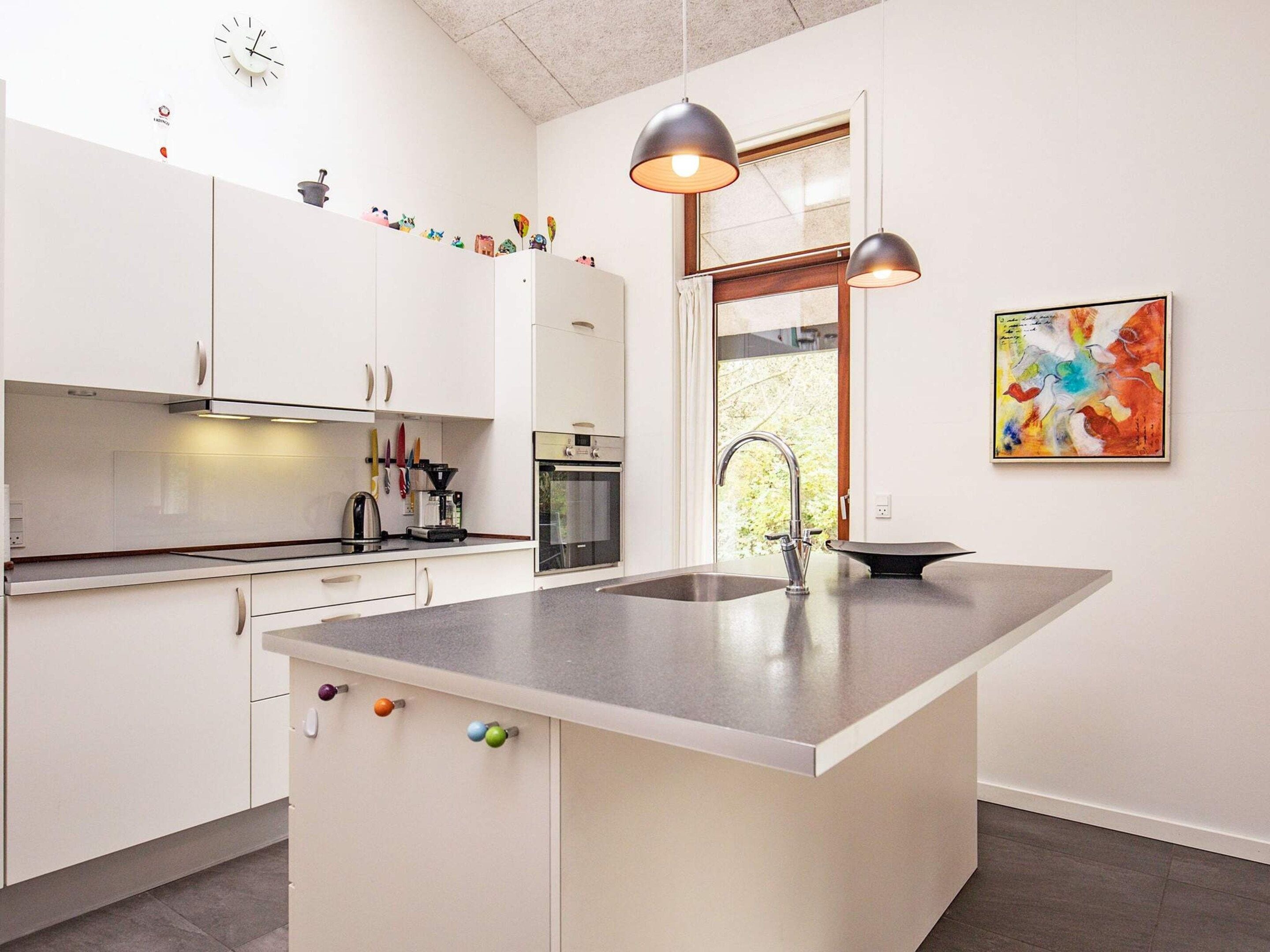 A modern kitchen with white cabinetry, a large island with a sink, pendant lighting, and a window with a view.